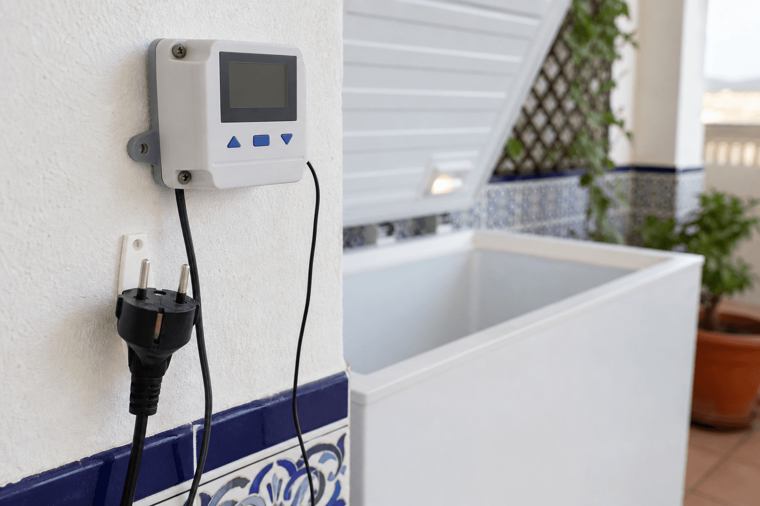 Controlador de temperatura junto a un arcón congelador abierto, con el enchufe europeo desenchufado y colocado en seco fuera de la bañera